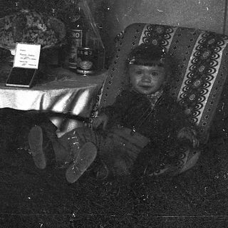 Vintage photo of child in traditional attire at table.