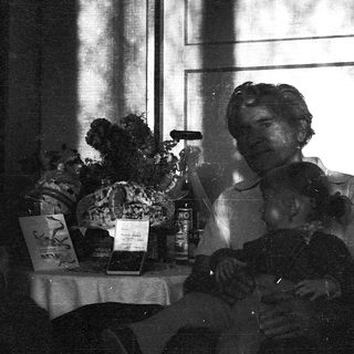 Black-and-white photo of two people seated indoors near a table with flowers and books.