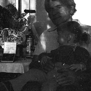 Black-and-white photo of two people seated indoors near a table with flowers and books.