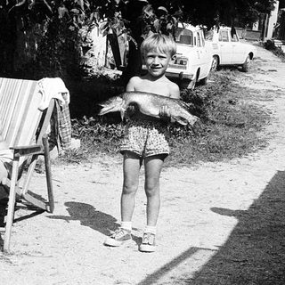 Child playing outside with adults relaxing nearby.