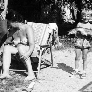 Child playing outside with adults relaxing nearby.