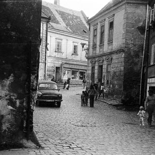 Historic cobblestone street with vintage car and pedestrians.