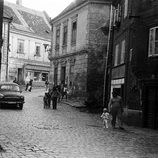 Historic cobblestone street with vintage car and pedestrians.