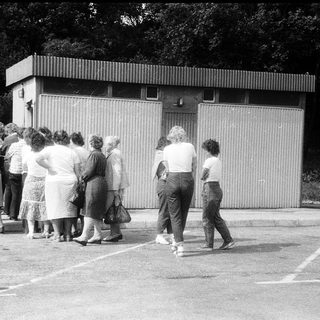 Group of people queuing outside a small building.