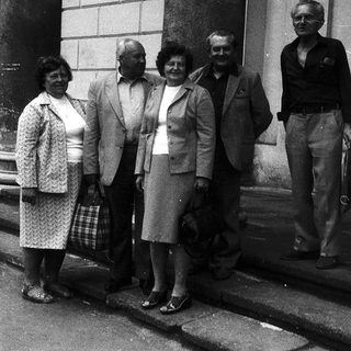 Five adults posing together outdoors in formal attire.