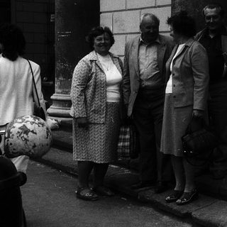 Group of people standing outside building in 1960s-70s attire.