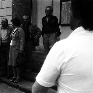 Group of people standing outside building in 1960s-70s attire.