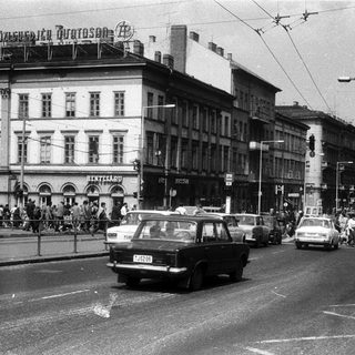 Busy urban street scene with vintage cars and pedestrians.