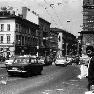 Busy urban street scene with vintage cars and pedestrians.