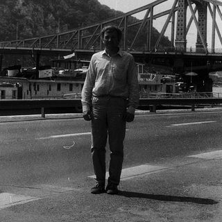 Man standing near bridge and hilltop monument.