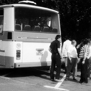 Group of people playing frisbee near parked bus.