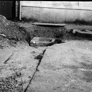 Excavated trench with exposed pipes and construction debris.