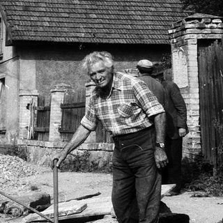 Old man inspecting damaged rural house ruins.