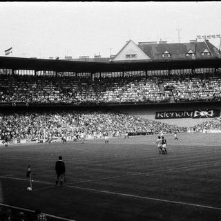Black-and-white stadium match with crowd and players.