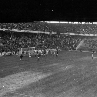 Football match in packed stadium at night.