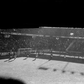 Football match in crowded stadium at night.