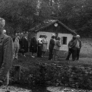 Group of people gathered near old stone wall and small wooden hut.