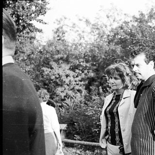 Two people standing outdoors in a wooded area.