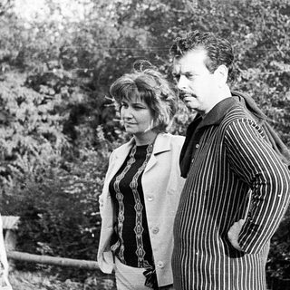 Two people standing outdoors in a wooded area.