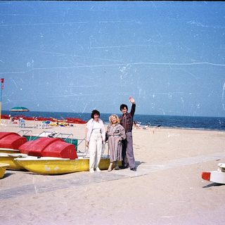Three people posing on beach near inflatable boats.