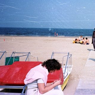 Beach scene with people relaxing and walking near boats.