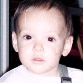 Young child in overalls holding yellow fabric.