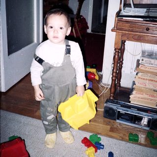 Young child in overalls holding yellow fabric.