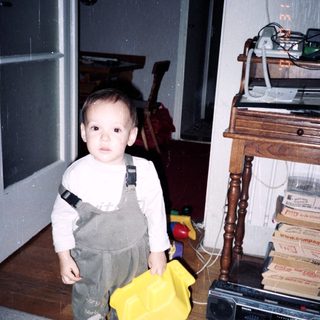 Young child in overalls holding yellow fabric.