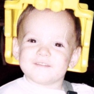 Child wearing yellow Lego helmet and overalls indoors.