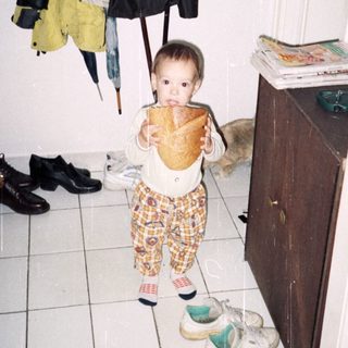 Baby standing in hallway mirror wearing diaper and holding stuffed animal.