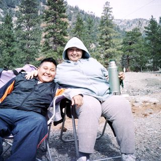 Two people posing happily outdoors in camping chairs.