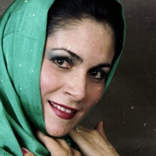 Woman wearing green headscarf and white top.