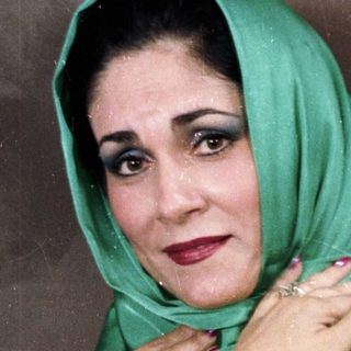 Woman wearing green headscarf and white sleeves.