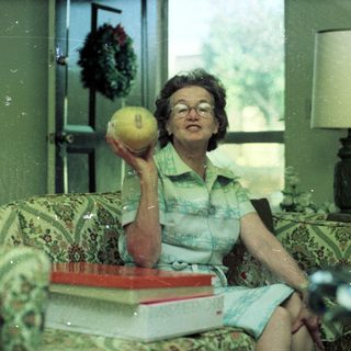 Woman holding tennis ball indoors, seated on floral couch.