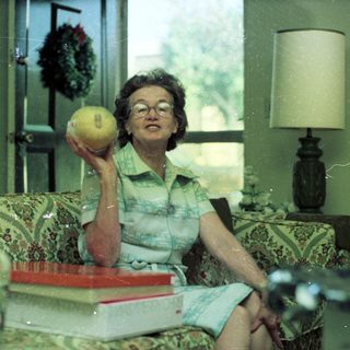 Woman holding tennis ball indoors, seated on floral couch.