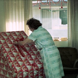 Woman ironing floral-patterned garment in vintage living room.