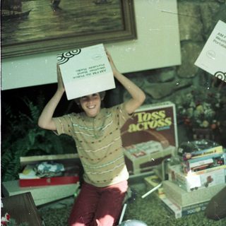 Two boys playfully balance boxes on their heads indoors.