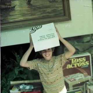 Two boys playfully balance boxes on their heads indoors.