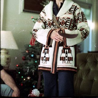 Woman wearing festive knit vest near Christmas tree.