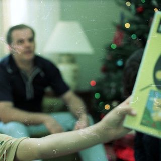 Young boy playing video game with adult in background.