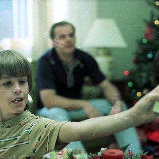 Young boy playing video game with adult in background.