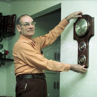 Man adjusting a wall clock in an office setting.