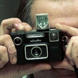 Man holding vintage camera, taking self-portrait indoors.