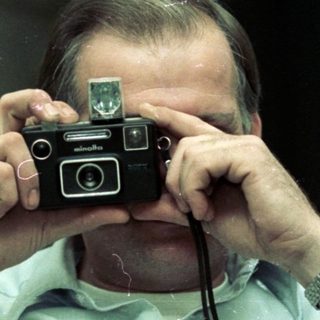 Man holding vintage camera, taking self-portrait indoors.
