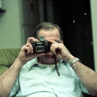 Man holding vintage camera, taking self-portrait indoors.