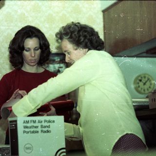 Two women handling vintage portable AM/FM weather radio.
