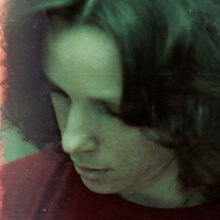 Person sitting indoors near window, looking downward.
