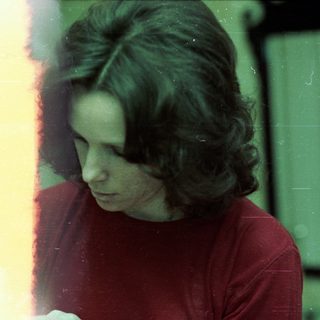 Person sitting indoors near window, looking downward.