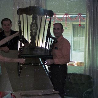 Three people posing with an old wooden rocking chair indoors.