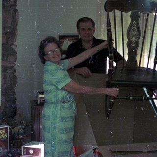 Three people posing with an old wooden rocking chair indoors.